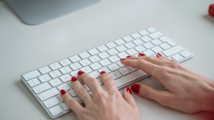 Closeup of the hands with red nails. Hands typing on the keyboard. Office work. White keyboard on white table. Work at home. Freelance.