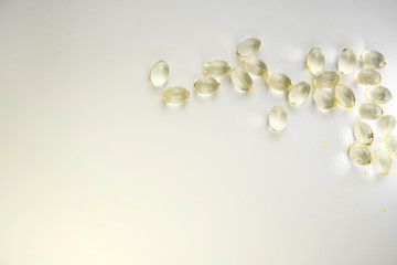 Vitamin D3 gelatin capsules on a white background. The fat-soluble solar vitamin cholecalciferol glows yellow and glistens. Place for text