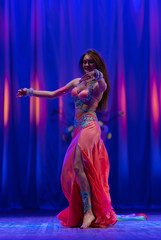Dancer with long hair in orange neon  oriental costumes dance belly dance on the concert stage