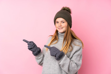 Ukrainian teenager girl with winter hat over isolated pink background pointing finger to the side