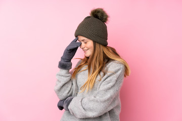 Ukrainian teenager girl with winter hat over isolated pink background laughing