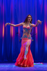 Dancer with long hair in orange neon  oriental costumes dance belly dance on the concert stage