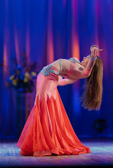 Dancer with long hair in orange neon  oriental costumes dance belly dance on the concert stage