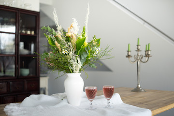 Edler Blumenstrauss in zarten Frühlingsfarben mit zwei vollen Weingläsern mit farblich passender...