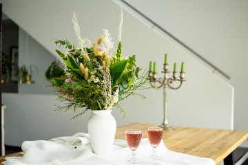 Edler Blumenstrauss in zarten Frühlingsfarben mit zwei vollen Weingläsern mit farblich passender Füllung in eleganter Umgebung
