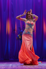 Dancer with long hair in orange neon  oriental costumes dance belly dance on the concert stage