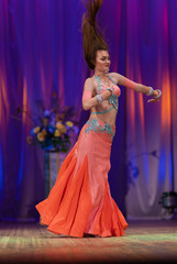 Dancer with long hair in orange neon  oriental costumes dance belly dance on the concert stage