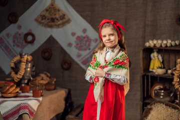 Little smiling girl wearing red headband and ornamental shawl smiling at camera standing near table with carnival feast