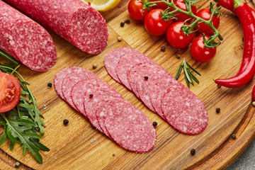 Traditional thinly sliced salami on a wooden cuttingboard  with spices, lettuce, avocado and tomatoes. Cold meat plate