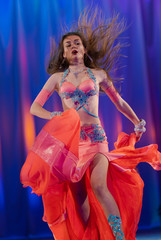 Dancer with long hair in orange neon  oriental costumes dance belly dance on the concert stage