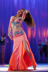 Dancer with long hair in orange neon  oriental costumes dance belly dance on the concert stage