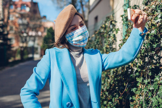 Woman wears reusable mask outdoors during coronavirus covid-19 pandemic. Girl taking selfie on empty street. Stay safe