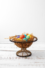 Fototapeta na wymiar Brightly Colored Easter Eggs in a Wire Basket on a White Wood Table