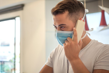A man wearing a protective mask against the COVID-19 virus calling his family from home.