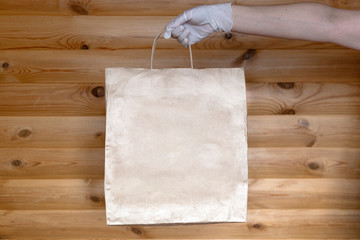 Hands in white medical gloves are holding paper bag with home delivery package.