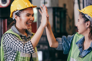 Happy cheerful female engineer or industrial technician worker giving high five to colleagues after work project success. woman wear protective hard hat in manufacturing factory. teamwork concept