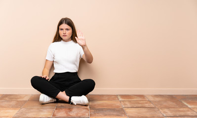Fototapeta premium Ukrainian teenager girl sitting on the floor making stop gesture
