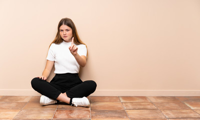 Ukrainian teenager girl sitting on the floor showing and lifting a finger