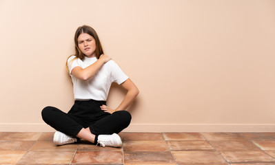 Fototapeta na wymiar Ukrainian teenager girl sitting on the floor suffering from pain in shoulder for having made an effort