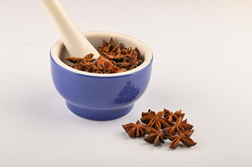 star anise in a blue ceramic spice mortar with a pestle on a white background. Close up.