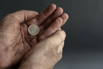One euro coin lies in dirty cupped hands of unemployed man on the dark background. Theme of job loss during the economic crisis.