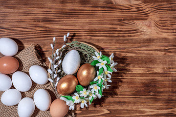 Fototapeta na wymiar Easter eggs in basket filled with straw and yellow flowers and willow on wooden rustic vintage background. Preparation for holiday. Easter decorations