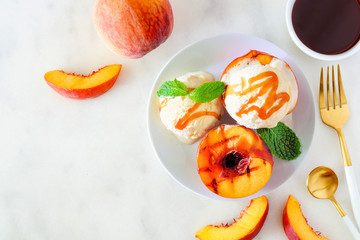 Sweet grilled peaches with vanilla ice cream and caramel sauce. Top view table scene on a white marble background.