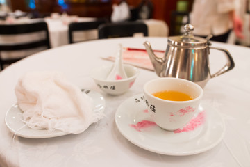 Tea service on a white table : Iron kettle, tea cup with hot tea, a soup bowl & special spoon. Beautiful typical chinese restaurant, Luk Yu Tea House, Central, Hong Kong, China.