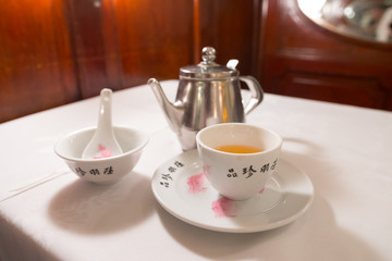 Tea service on a white table : Iron kettle, tea cup with hot tea, a soup bowl & special spoon. Beautiful typical chinese restaurant, Luk Yu Tea House, Central, Hong Kong, China.