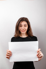 young brunette woman in a black t-shirt smiling shows a white sheet on a white background. copyspase