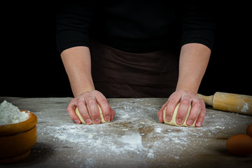 Man hands kneading bread dough on a wooden table with black background