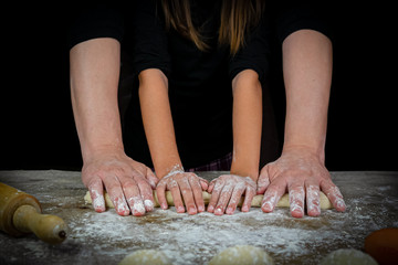 Hands of man and girl kneading bread dough on a wooden table with black background