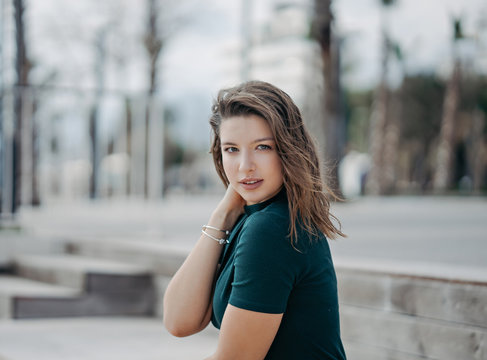 A beautiful young brunette girl is walking in the city posing for the camera. Sunny weather and promenade in Antalya