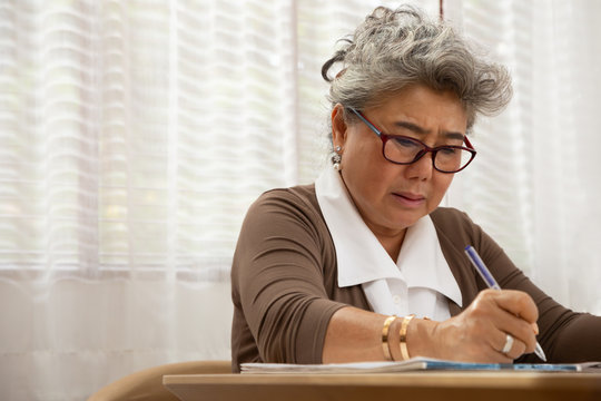 Asian senior woman serious writing down letters on a piece of paper, Work from home or stay home concept