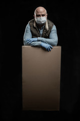 A man in a medical mask and gloves with a big box in his hands. Delivery and quarantine period of the coronavirus pandemic. Precautions. Black background. Vertical.