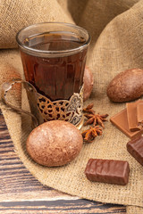 A faceted glass of tea in a vintage Cup holder, chocolate gingerbread, chocolate and star anise on a background of rough homespun fabric. Close up.