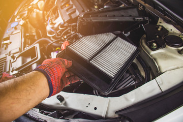 Car air filter in a hand of mechanic man is installing into air filter socket of car...
