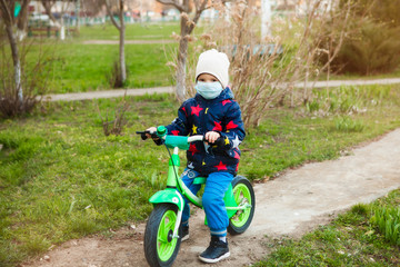 Fototapeta premium quarantine. A boy in a medical mask on a runbike walks along the street near the house during quarantine of the coronavirus. The ability to go for a walk with safety measures