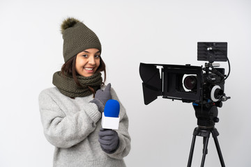 Obraz premium Reporter woman holding a microphone and reporting news over isolated white background pointing back