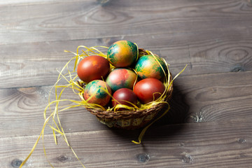 colorful easter eggs in basket nest on brown wooden background