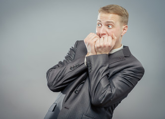 Closeup portrait of a scared guy biting his fist against white background