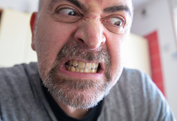 Portrait of an extremely angry middle-aged Caucasian man: bloodshot eyes are staring down at the side. The gritted teeth and the curled nose in the expression of anger. Blurry background