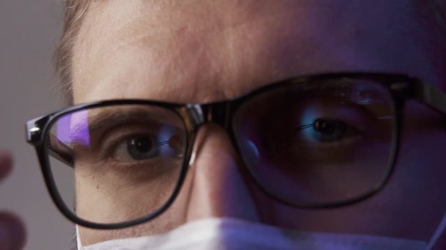 Macro: A man wearing glasses and a mask scornfully looks into the camera and takes off his glasses