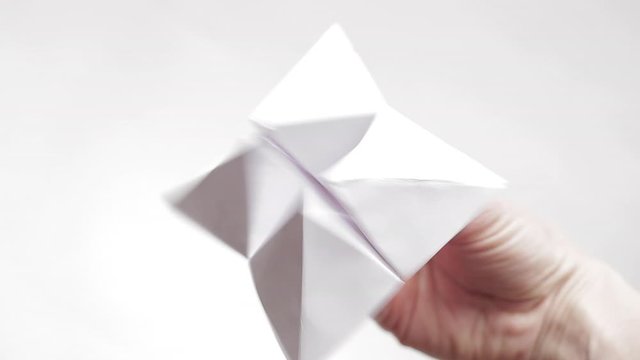 in the hands of a woman an origami figure from white paper in the form of volumetric triangles, an envelope for fingers, a woman deforms this figure