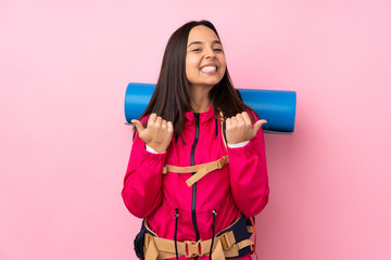 Young mountaineer girl with a big backpack over isolated pink background with thumbs up gesture and smiling