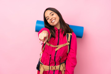 Young mountaineer girl with a big backpack over isolated pink background points finger at you with a confident expression