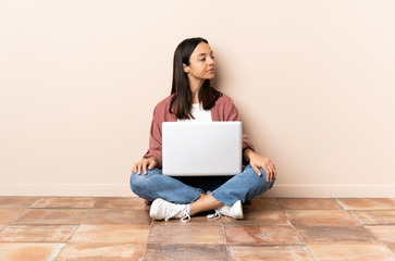 Young mixed race woman with a laptop sitting on the floor looking to the side