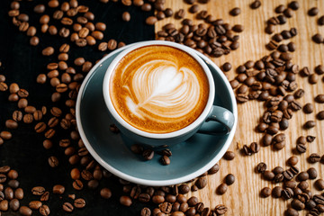 Gray cup of coffee on the black and brown table among spilled roasted coffee beans. Cappuccino with cofee art in the cafe.