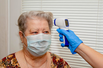 A doctor in blue latex gloves measures the body temperature with an infrared emitter in a woman...
