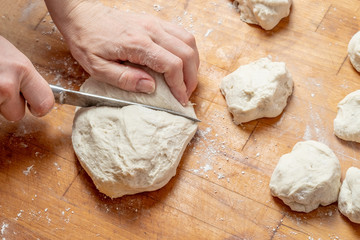 Female hands cut with a knife a kneaded dough on a wooden table.